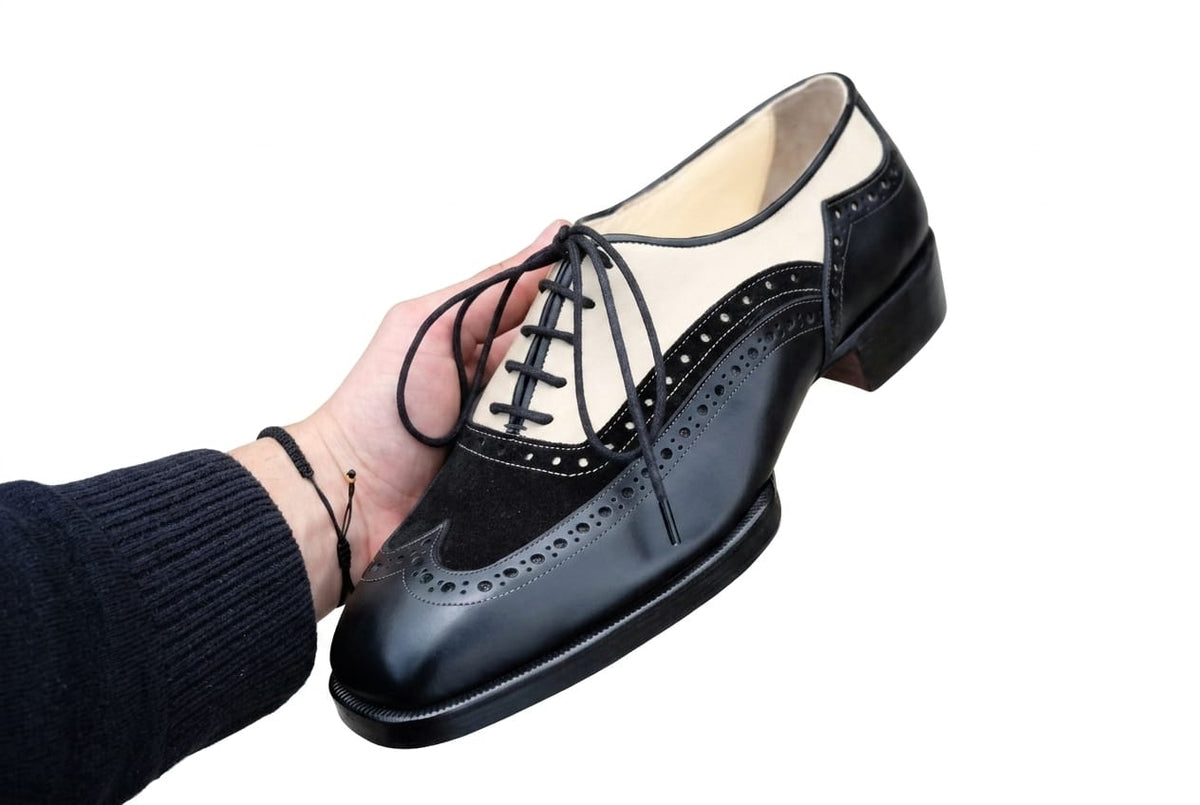 Black leather shoe with brogue details held by a hand on a white background