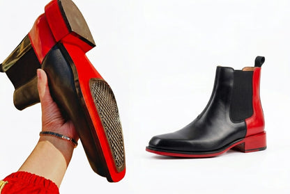 Black and red Chelsea boots with a hand holding one boot showing sole texture.